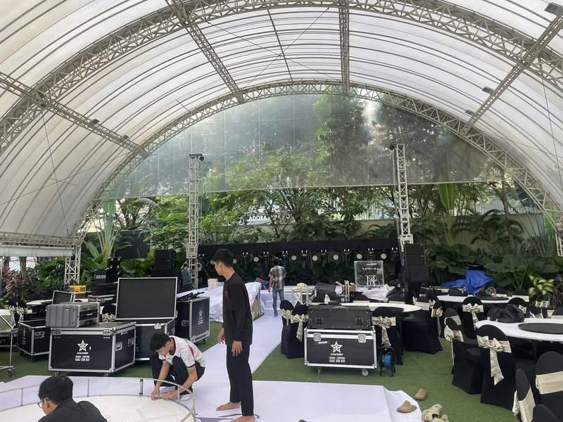 Nhân viên đang lắp đặt thiết bị âm thanh ánh sáng dưới mái vòm lớn chuẩn bị cho sự kiện ngoài trời