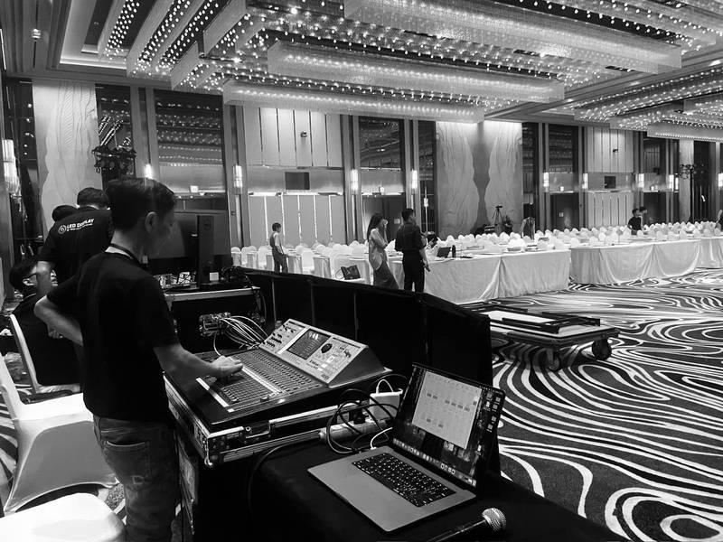Người kỹ thuật viên điều khiển bàn mix âm thanh trong một hội trường sự kiện lớn với hệ thống ánh sáng và âm thanh chuyên nghiệp