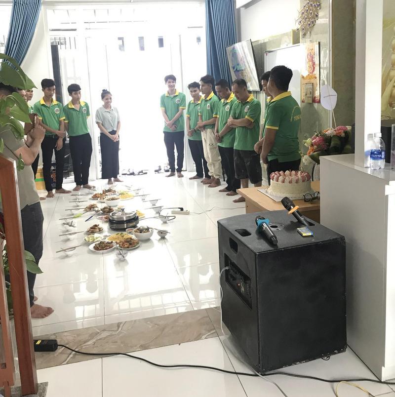 Nhóm người trong trang phục đồng phục đứng xung quanh mâm thức ăn trong phòng với loa kẹo kéo và micro, thể hiện dịch vụ cho thuê loa kẹo kéo