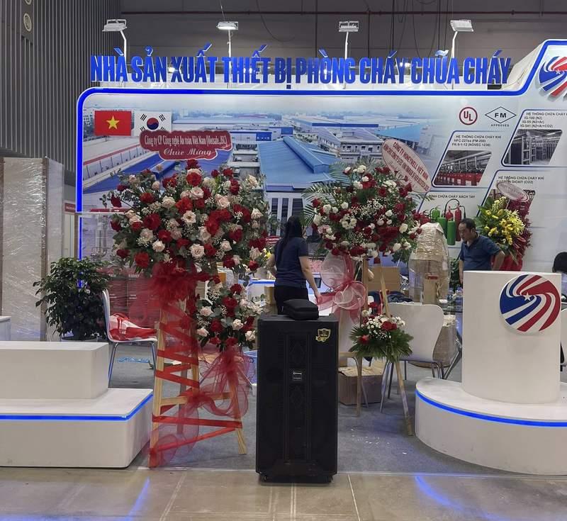 Loa kẹo kéo đứng giữa gian hàng triển lãm với hoa tươi trang trí, thể hiện dịch vụ cho thuê loa kẹo kéo phục vụ sự kiện.