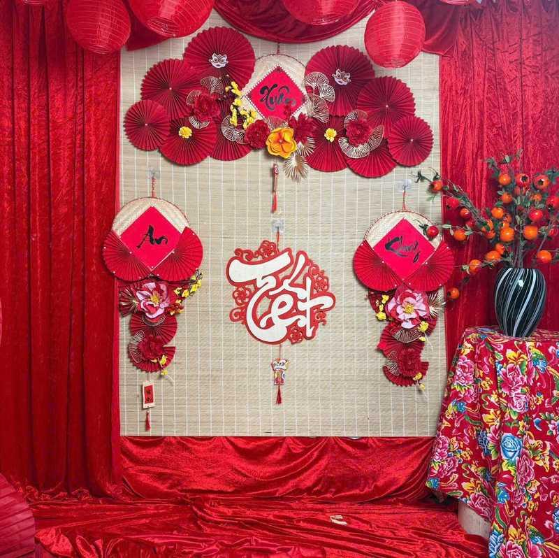 Dịch vụ trang trí Tết thi công tiểu cảnh Tết trọn gói với hoa giấy đỏ và chữ thư pháp trên nền tre.