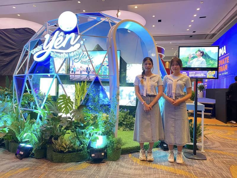 Hai nhân viên đứng chụp ảnh tại gian hàng sự kiện trong dịch vụ tổ chức activation trọn gói của agency activation uy tín.