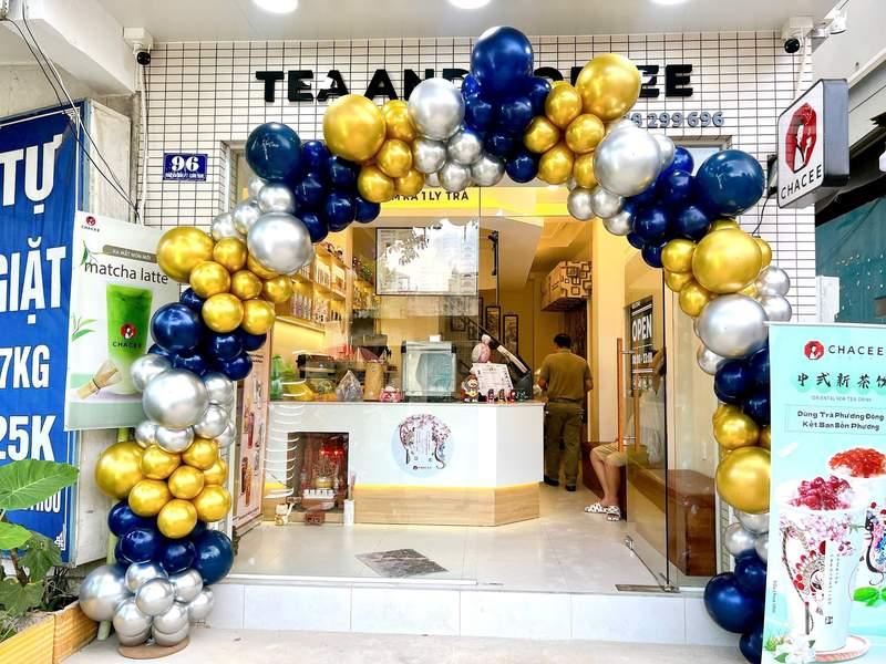 Trang trí bóng bay sự kiện với cổng bóng vàng, xanh và bạc tạo điểm nhấn sân khấu và backdrop trọn gói tại cửa hàng trà sữa.