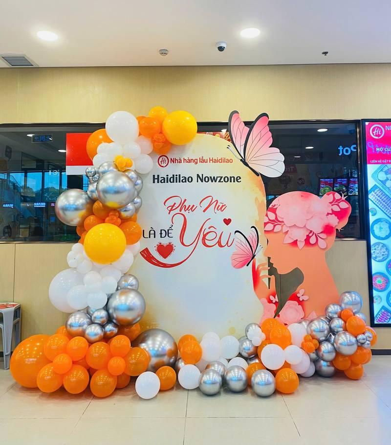 ALT: Tiểu cảnh trang trí ngày phụ nữ công ty với bóng bay cam, trắng, bạc và backdrop 8/3, 20/10 văn phòng sang trọng.