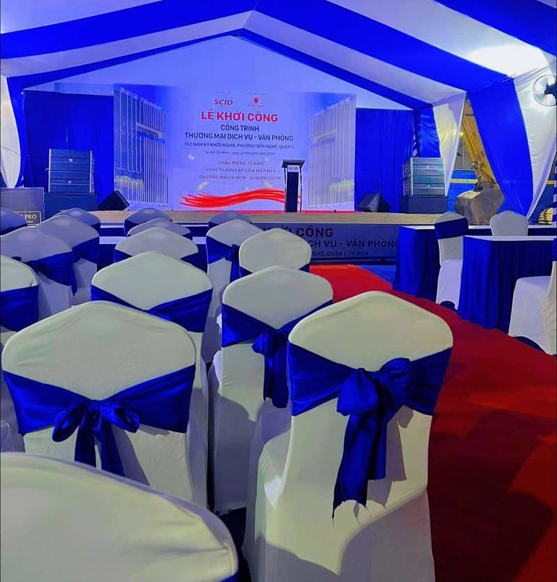 Trang trí sân khấu sự kiện với thiết kế ghế trắng thắt nơ xanh và backdrop hiện đại tại HCM.